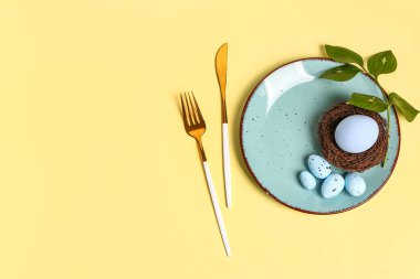 Table serving with Easter eggs and green plant branch on yellow background