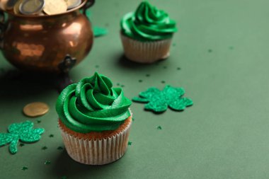 Tasty cupcakes for St. Patrick's Day, clovers and pot of coins on green background