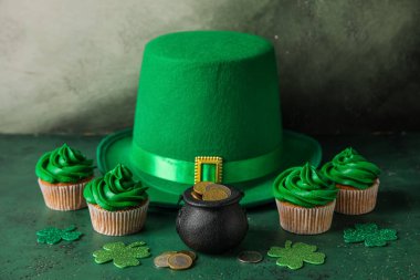 Tasty cupcakes for St. Patrick's Day, leprechaun hat and pot of coins on green table near grunge wall