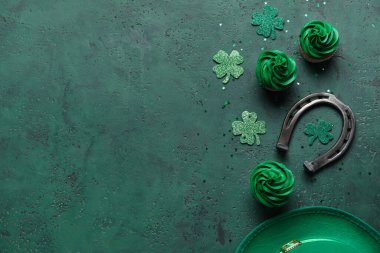 Tasty cupcakes for St. Patrick's Day, horseshoe and clovers on green background