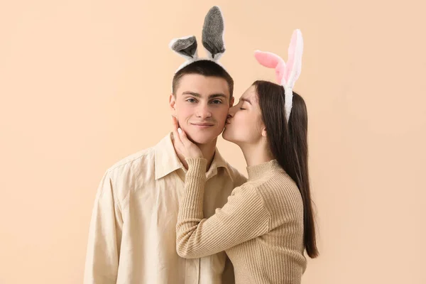 Young woman in bunny ears kissing her boyfriend on beige background. Easter celebration