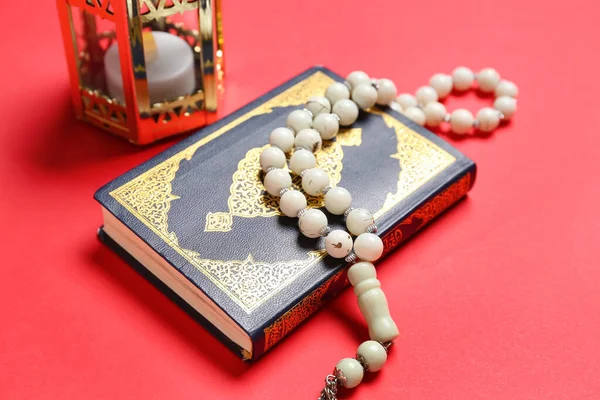 Koran with prayer beads and Muslim lantern for Ramadan on red background, closeup