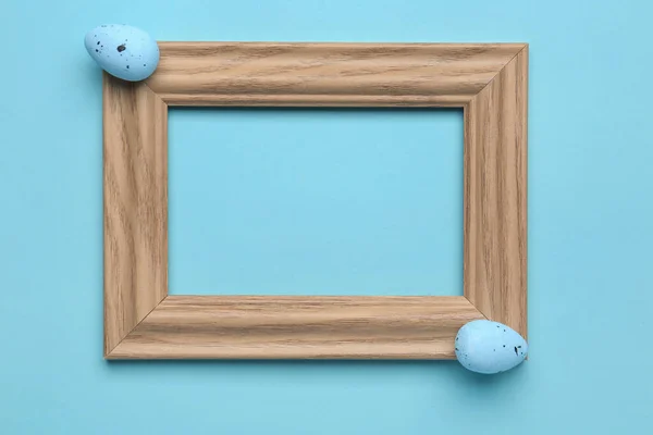 Empty picture frame and Easter eggs on color background
