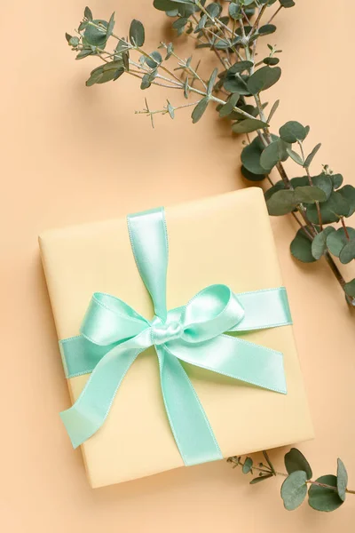 Gift box and eucalyptus branches on orange background. Hello spring