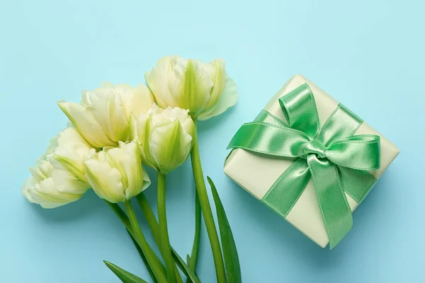 Gift box and beautiful tulip flowers on blue background. Hello spring