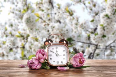 Alarm clock and flowers on table outdoors. Spring time