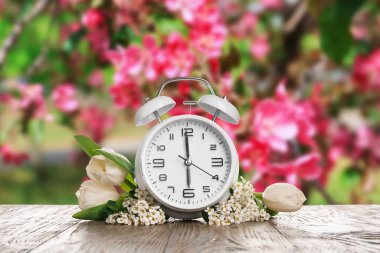 Alarm clock and flowers on table outdoors. Spring time