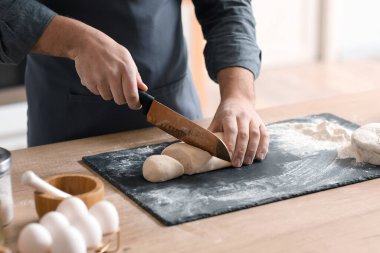 Male baker cutting dough at table in kitchen, closeup