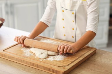 Little baker rolling out dough at table in kitchen, closeup