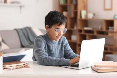 Little boy in eyeglasses using laptop at home