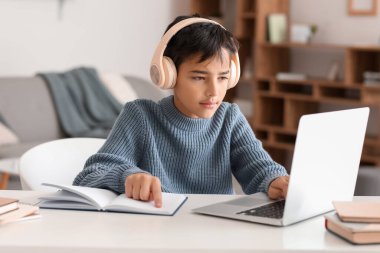 Little boy in headphones with book using laptop at home