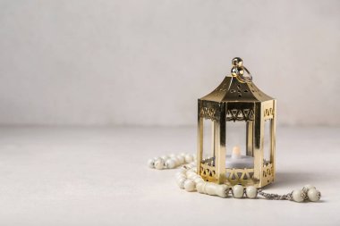 Muslim lantern with candle and prayer beads for Ramadan on light background