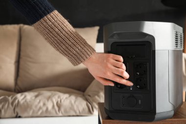 Woman turning on portable power station at home, closeup