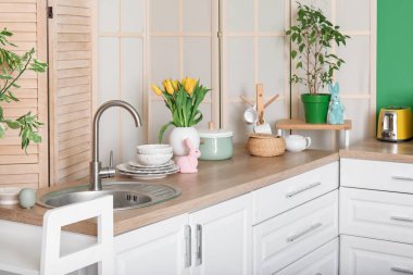 Interior of stylish kitchen with Easter rabbits, tulips in vase and white counters