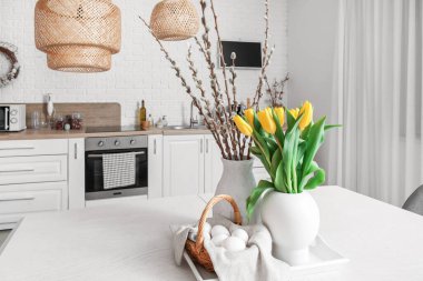 Vases with tulips, willow branches and Easter eggs on dining table in kitchen