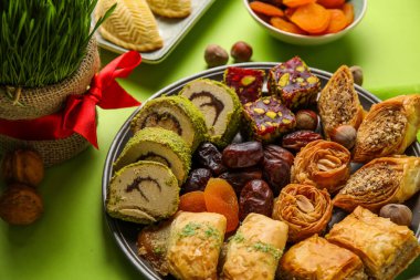 Plate with treats and grass on green background, closeup. Novruz Bayram celebration