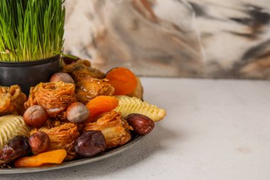 Plate with treats and grass on table near grunge wall, closeup. Novruz Bayram celebration