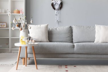 Vase with tree branches, Easter eggs and rabbit on table in interior of living room