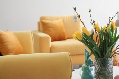 Vase with tulips, Easter eggs and rabbit on table in living room