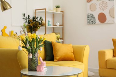 Vase with tulips, Easter eggs and rabbit on table in living room