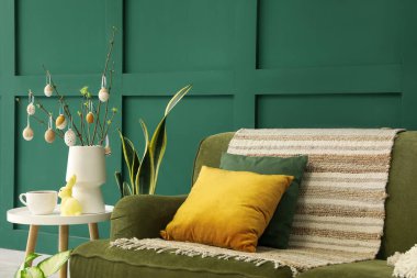 Vase with tree branches, Easter eggs, rabbit and cup on table in living room