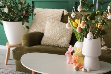 Vases with tulips, tree branches, Easter eggs and rabbits on table in living room