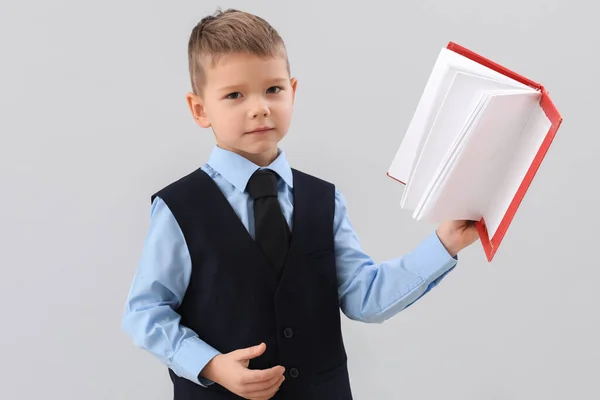 Cute little teacher with book on grey background