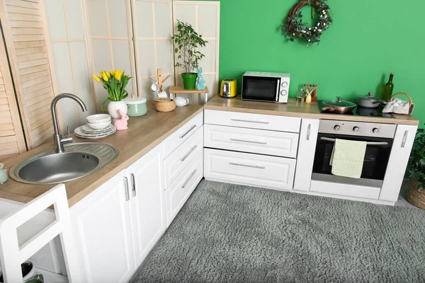 Interior of stylish kitchen with Easter wreath, rabbits and white counters