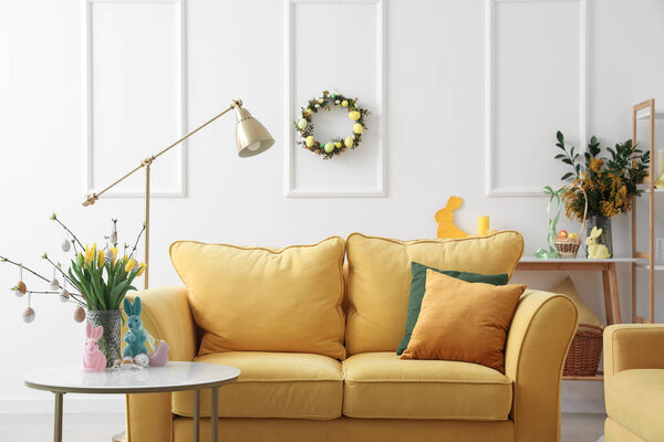 Interior of living room with yellow sofa, flowers and Easter eggs