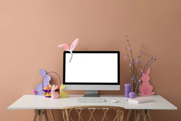 Workplace with computer, tree branches and Easter eggs in vase near color wall