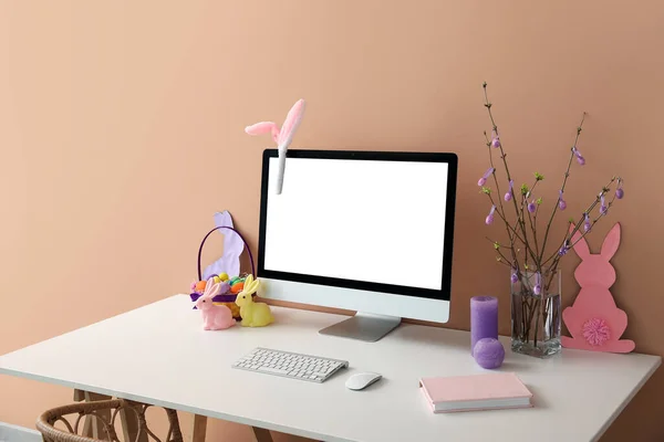 Workplace with computer, tree branches and Easter eggs in vase near color wall