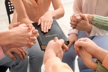 Group of people praying with Holy Bible in room, closeup