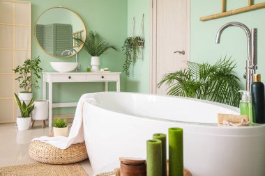 Interior of bathroom with modern bathtub, aroma candles and houseplants