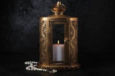 Muslim lantern with burning candle and prayer beads for Ramadan on dark background