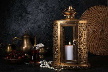 Muslim lantern with tasbih, dates and glass of tea for Ramadan on dark background