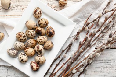 Plate with Easter eggs and willow branches on light wooden background