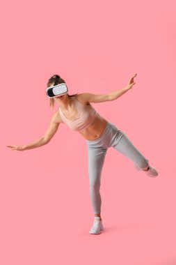 Pretty young woman in VR glasses on pink background