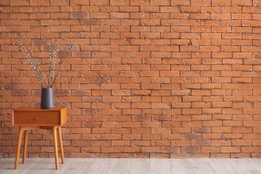 Vase with pussy willow branches on table near brick wall