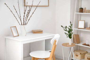 Workplace with willow branches in vase and frame near light wall