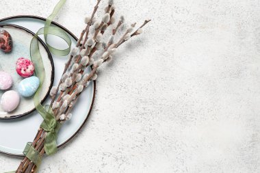 Plate with painted Easter eggs and willow branches on light background