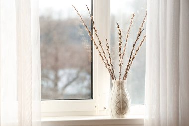 Vase with pussy willow branches on windowsill in room