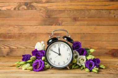 Composition with beautiful eustoma flowers and alarm clock on wooden background