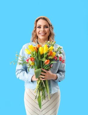 Beautiful happy young woman with bouquet of tulips on light blue background