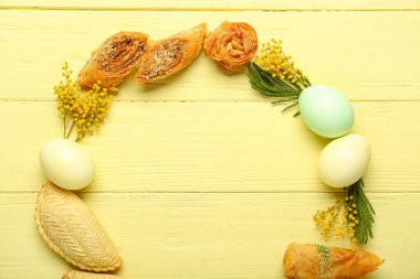 Frame made of flowers, eggs and treats on yellow wooden background. Novruz Bayram celebration