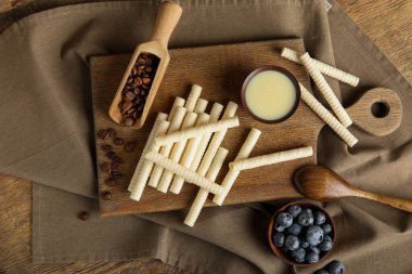 Board with delicious wafer rolls, blueberries and condensed milk on wooden background