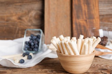 Bowl with delicious wafer rolls on wooden background