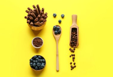 Composition with delicious chocolate wafer rolls, blueberries and coffee beans on yellow background