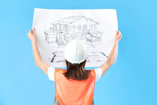 Female engineer with drawing on blue background, back view