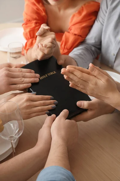 Group of people praying with Holy Bible before dinner at table, closeup