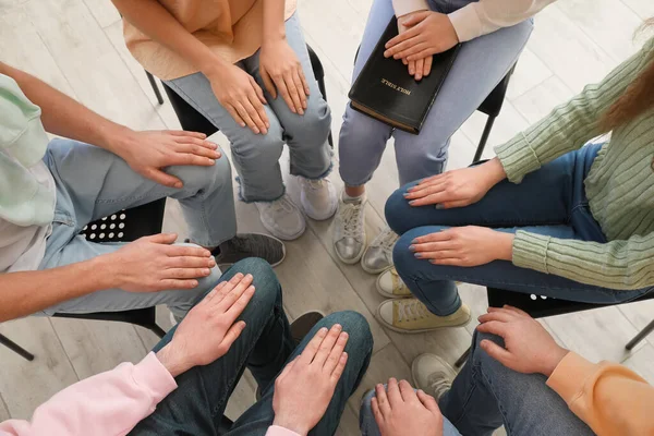 Group of people praying with Holy Bible in room, top view